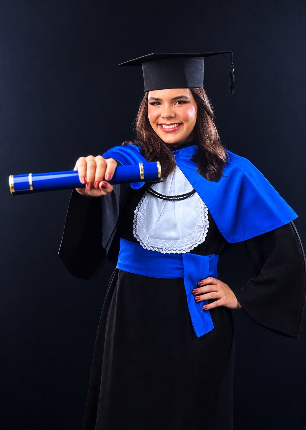 Giovana de beca, sorrindo, com o canudo azul na mão
